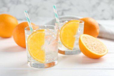 Portakal dilimli maden suyu ve beyaz ahşap masada taze meyveler, yakın plan.