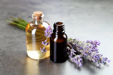 Şişelerdeki yağlar ve gri desenli masadaki lavanta çiçekleri, yakın plan.