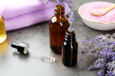 Şişelerdeki yağlar, damlacıklar ve lavanta çiçekleri gri desenli masada, yakın plan.