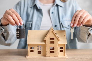 Ev güvenliği. Evin modeli, anahtarı ve asma kilidi olan kadın ahşap masada, yakın plan.