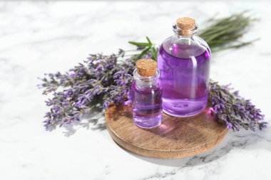 Beyaz mermer masa üzerinde lavanta çiçekleri ve şişelerdeki yağlar yakın plan.