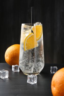 Portakal dilimleri ve siyah ahşap masadaki buz küpleriyle soda tazeleniyor.