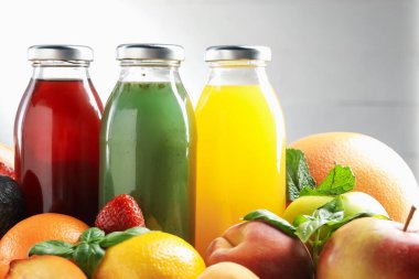 Cam şişelerdeki lezzetli sıvılar, taze malzemeler ve açık gri arka plana karşı fesleğen, yakın plan.