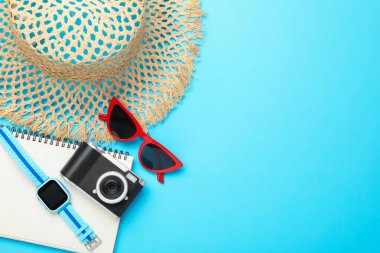 Yaz tatili zamanı. Kamera, akıllı saat, dizüstü bilgisayar ve açık mavi arka planda plaj aksesuarları, düz yatış. Metin için boşluk