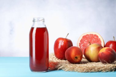 Cam şişede lezzetli meyve suyu ve açık mavi ahşap masada taze meyve.