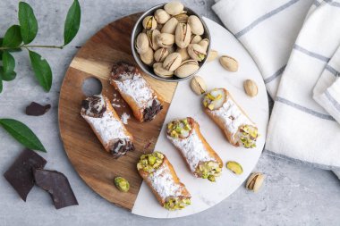 Lezzetli cannoli, ricotta peyniri, fıstık, çikolata ve pudra şekeri, gri mermer masa, düz uzanmış