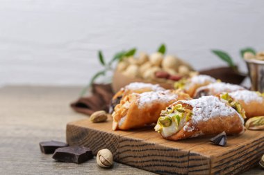Ricotta peynirli, fıstıklı, fıstıklı, fıstıklı, çikolatalı ve pudra şekerli nefis cannoli, açık gri arka planda, yakın plan.