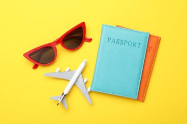 Yaz tatili zamanı. Oyuncak uçak, pasaport ve güneş gözlüğü sarı arka planda, düz konum