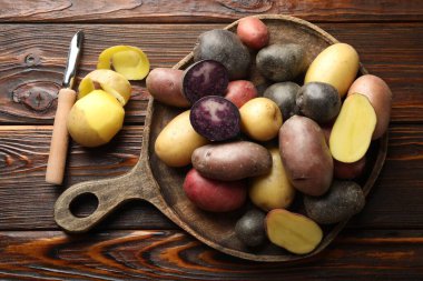 Tahta masa üzerinde farklı patates ve soyucu türleri, düz yatıyordu.