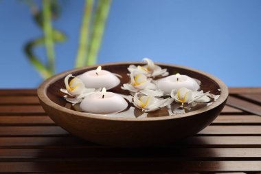 Yanan mumlar ve orkide çiçekleri ahşap masadaki su kasesinde bulanık mavi arka planda, yakın plan