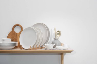 Temiz bulaşık takımı ve tahta kesme tahtası beyaz duvarın yanında.