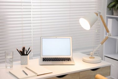 Ofisteki beyaz masada dizüstü bilgisayarı ve kırtasiyesi olan şık bir iş yeri.