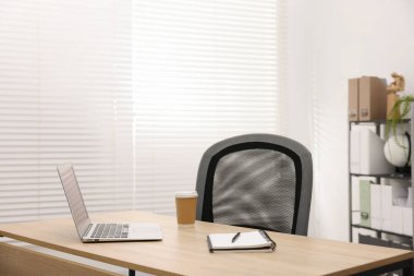 Ofisteki ahşap masada dizüstü bilgisayarı, kahvesi ve kırtasiyesi olan şık bir iş yeri.