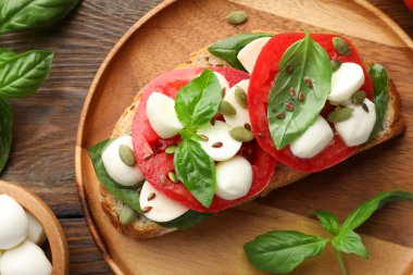 Peynirli, domatesli, ahşap masadaki fesleğenli lezzetli sandviç.