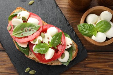 Peynirli, domatesli, ahşap masada fesleğenli lezzetli bir sandviç.