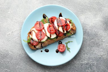 Mozarella peynirli lezzetli sandviç, balzamik sos, domates ve roka gri masada, üst görünümde.