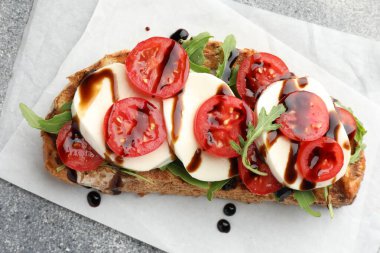 Mozarella peynirli lezzetli sandviç, balzamik sos, domates ve roka gri masada, üst görünümde.