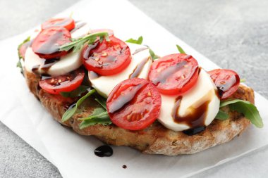 Mozarella peynirli lezzetli sandviç, balzamik sos, domates ve roka gri masada, yakın plan.