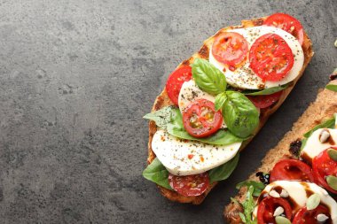 Mozarella peynirli lezzetli sandviçler ve gri masada domatesler, düz yatak. Metin için boşluk