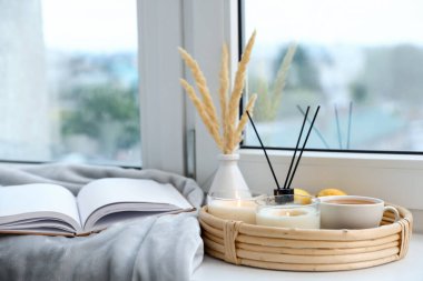 Yanan mumlarla kaplıca kompozisyonu ve pencere pervazında kamış oda spreyi.