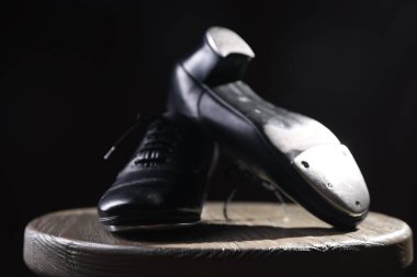 Siyah arka planda tahta taburede step dansı için bir çift ayakkabı, yakın plan.