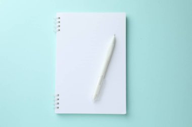 Açık mavi arkaplanda beyaz defter ve kalem, üst görünüm