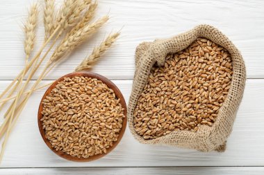 Kase içinde buğday taneleri, çuval bezi torbası ve beyaz ahşap masada çivili kazıklar, düz uzanmış.