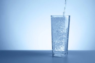 Masadaki ferahlatıcı soda suyunu açık mavi gradyan arkaplana yakın çekim yaparak bardağa döküyorum. Metin için boşluk