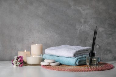 Gri duvarın yanındaki beyaz ahşap masada yanan mumlarla kaplıca kompozisyonu