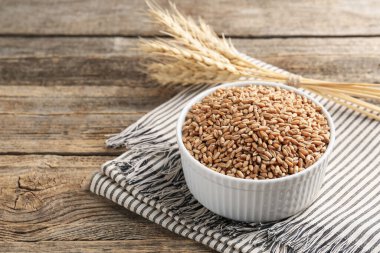 Kase içinde buğday taneleri ve tahta masada çiviler, yakın plan. Metin için boşluk