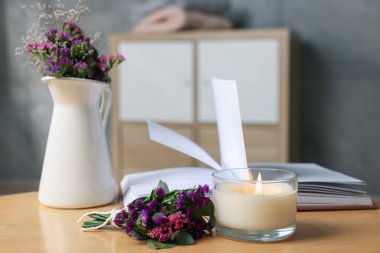 Yanan mum, açık kitap ve çiçekler kapalı bir masada, yakın plan.