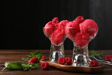 Tatlı kaselerinde nefis ahududu şerbeti, nane ve taze böğürtlen ahşap masada siyah arka planda, yakın planda.