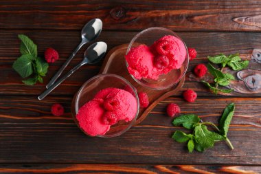 Tatlı kaselerinde nefis ahududu şerbeti, kaşıklar, nane ve taze böğürtlen ahşap masada, düz uzanmış