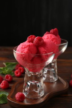 Tatlı kaselerinde nefis ahududu şerbeti, nane ve taze böğürtlen ahşap masada siyah arka planda, yakın planda.