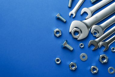 Metal anahtarlar, fındıklar ve cıvatalar mavi arka planda, düz yerde. Metin için boşluk