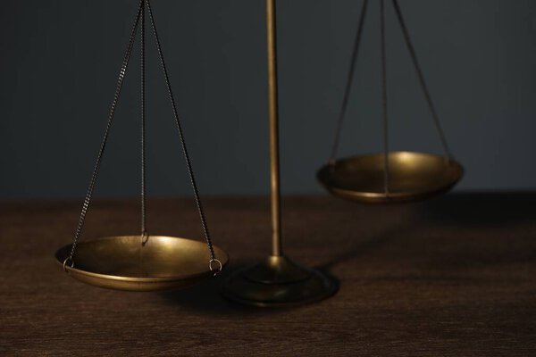 Весы правосудия на деревянном столе на сером фоне, крупный план