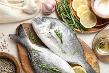 Taze çiğ dorado balığı, limon dilimleri, biberiye ve baharatlar beyaz ahşap masa, düz yatak. Organik deniz ürünleri