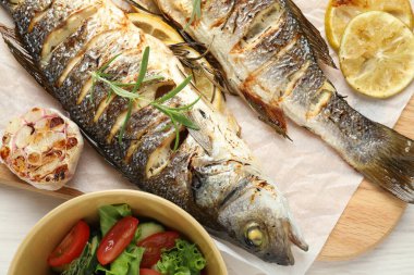 Beyaz ahşap masada salata ve limonla servis edilen lezzetli kavrulmuş deniz kabuğu balığı. Ev yapımı deniz ürünleri yemeği.