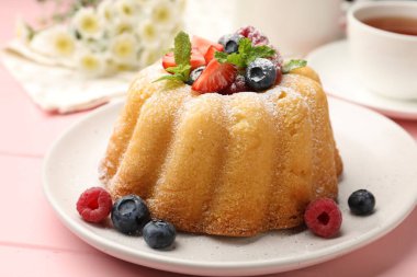 Pudra şekerli, böğürtlenli ve nane şekerli nefis kek, pembe ahşap masa, yakın plan.