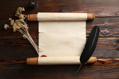 Yuvarlanmış parşömen, tüy, kuru çiçekler ve tahta masa üzerine mürekkep.