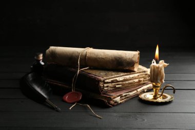 Eski parşömen, yanan mum, tüy ve kitaplar siyah ahşap masada.