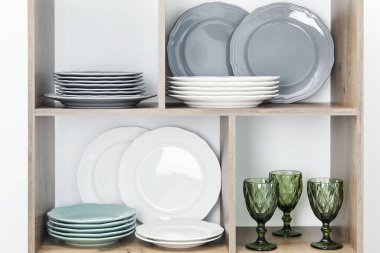 Beyaz duvarın yanında farklı plakalar ve gözlüklerle raf ünitesi.