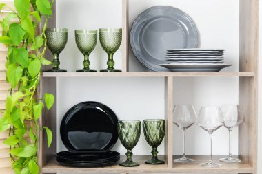 Beyaz duvarın yanında farklı bulaşık takımları, gözlük ve çiçek dekoru olan raf ünitesi.