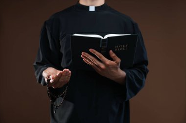 Kahverengi arka planda kutsal kitabı ve tespihi olan rahip, yakın plan.