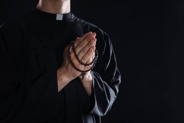 Siyah arka planda tespih çeken bir rahip, yakın plan. Metin için boşluk