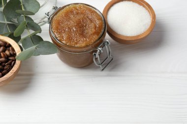 Cam kavanozda doğal vücut fırçası ve beyaz ahşap masa üzerindeki malzemeler. Metin için boşluk