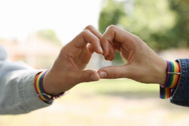 LGBT konsepti. Gökkuşağı bileklikli kadınlar açık havada kalp şekillendiriyor, yakın plan.