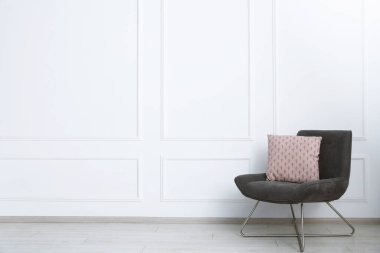 Beyaz duvarın yanında yastıklı rahat koltuk, metin için boşluk.