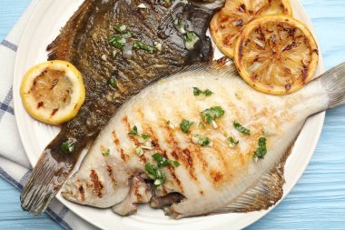 Açık mavi ahşap masa üzerinde limon dilimleri ve otlarla kızartılmış balık, yakın plan. Ev yapımı deniz ürünleri yemeği.