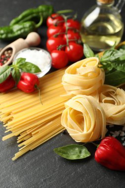 Farklı türde makarna ve malzemeler siyah masada, yakın plan.